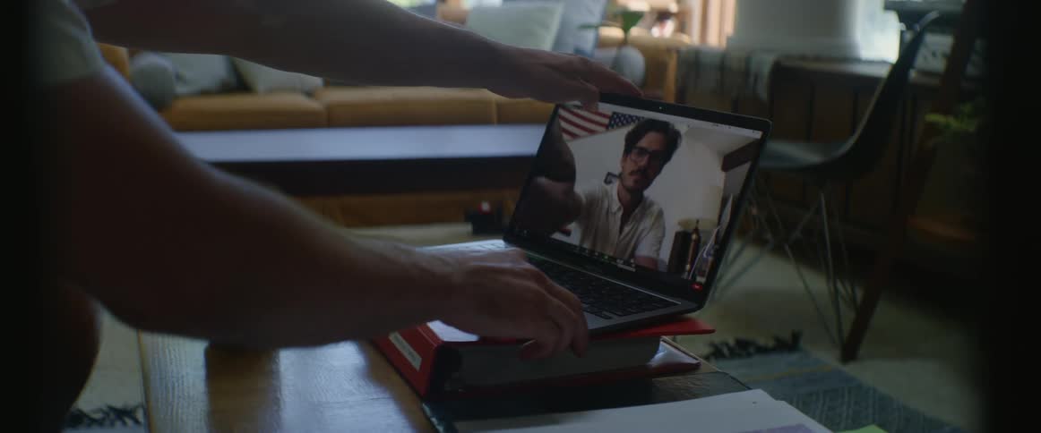 A man with glasses sitting on a couch next to a table and opening a laptop