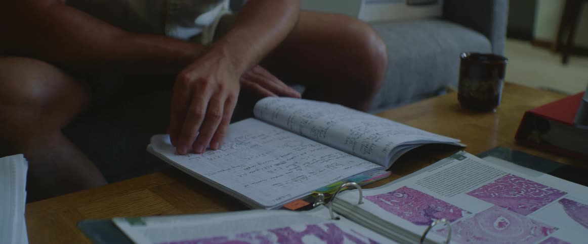A man is sitting on a couch leafing through a notebook with notes