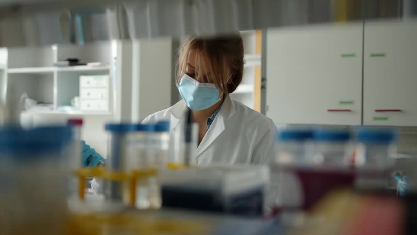 A woman working in a lab puts a test tube in a tray after she puts liquid in it