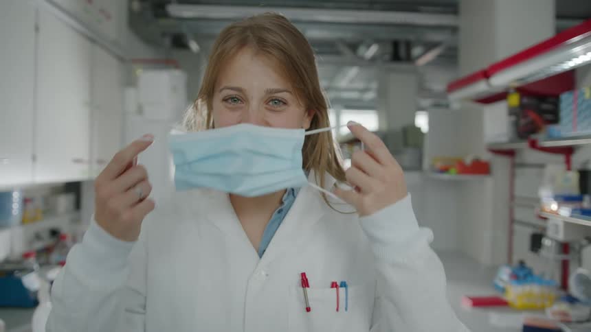 A woman working in a lab takes her mask off and smiles