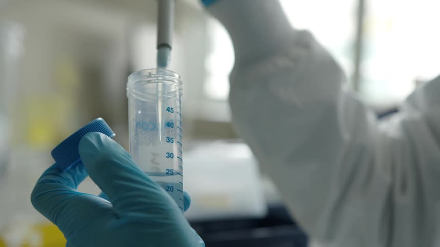 A person in a lab takes liquid out of a container
