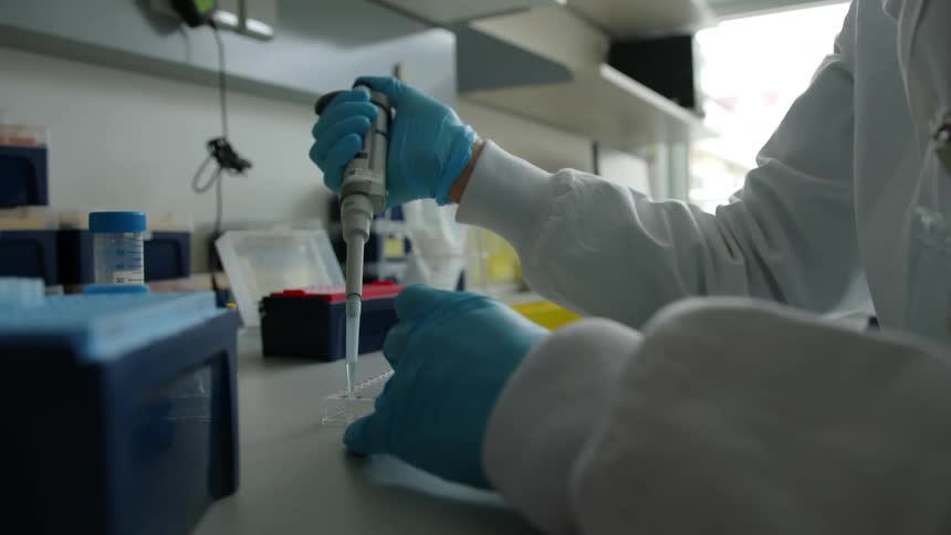 A woman in a lab puts liquid in a tray