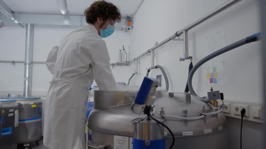 A man with goggles a mask and gloves and a lab coat taking a rack out of a tank of liquid nitrogen
