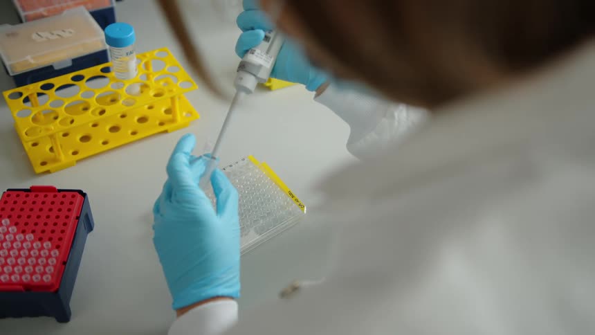 A woman sits at a table with samples and trays wearing a face mask and gloves