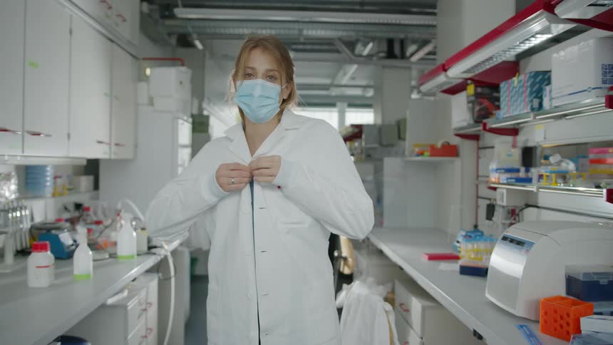 A woman in a lab puts her lab coat on