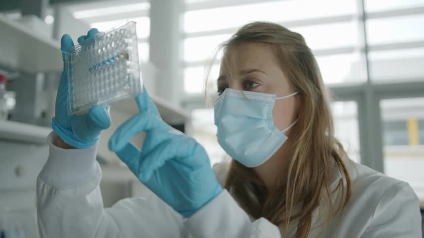 A female lab technician looks and points at a sample tray in a laboratory setting