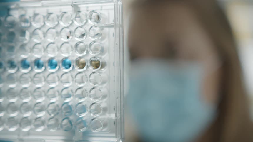 A lab worker holds up a tray in front of her face to examine it
