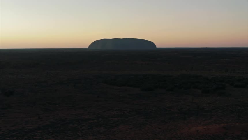 Rock formations and the silhouette of a butte on the horizon at sunset