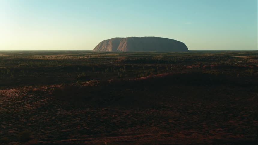 Aerial pushes in and tilts up to reveal Australia's Uluru at sunrise