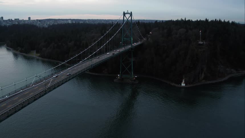 Vehicles travel on Lions Gate Bridge over the ocean into Stanley Park forest