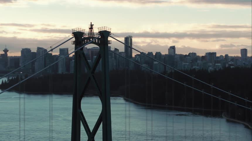 Lions Gate Suspension Bridge spans water to connect to forest covered shoreline near downtown Vancouver city