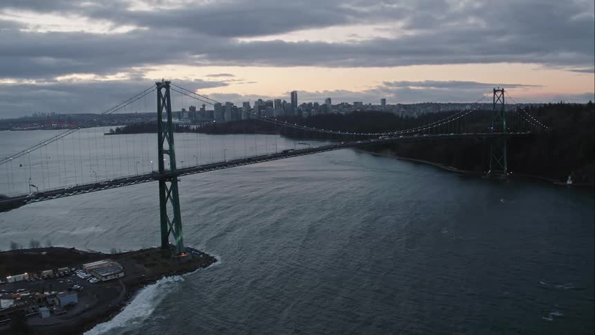 Lions Gate Bridge spans water with Vancouver sunrise in horizon
