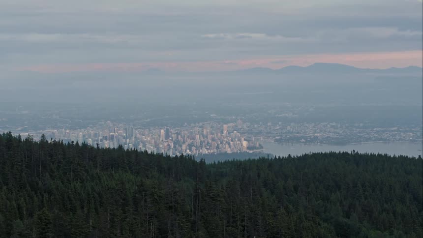 A distant downtown Vancouver is revealed from a forested mountain