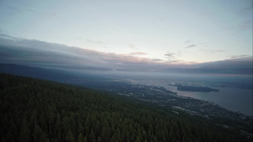 Aerial push in displaying forested mountain and distant Vancouver city