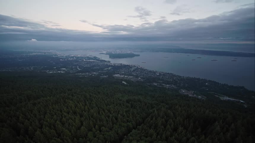 Aerial pulls back up forested mountain showing Vancouver in distance
