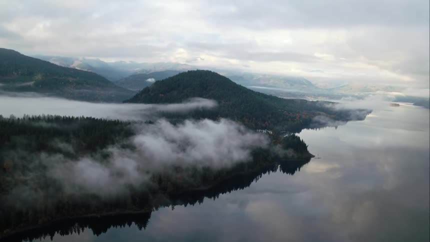 Clouds and fog hang over forested mountain range with large lake