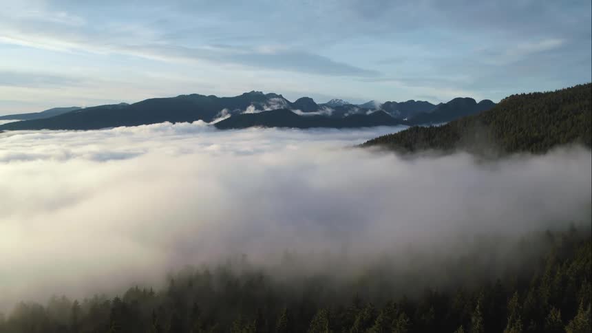 High alpine aerial of fog hanging over forests and mountains