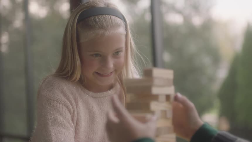 A blonde girl watches another child complete a piece to a game and smiles in anticipation