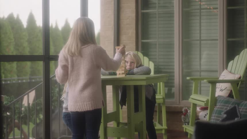 Three blonde siblings play a block stacking game on their screened in patio