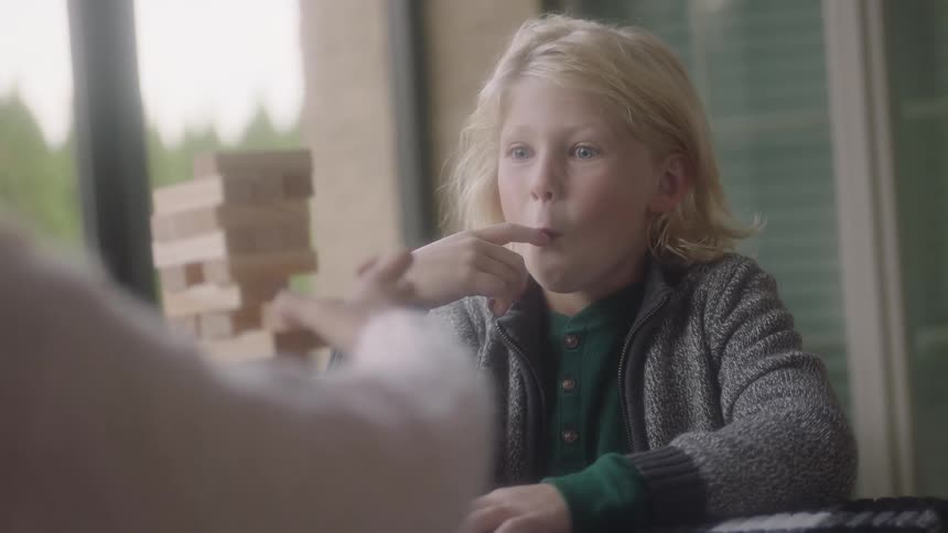 A boy tries to distract his sister by putting a finger in his mouth as they play a stacking game