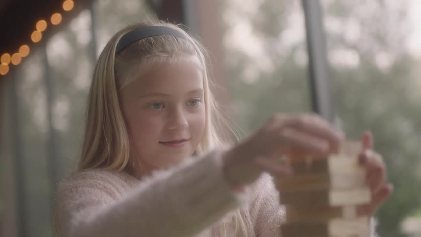 Little girl placing a wooden block at the top of a stacked wooden block tower game