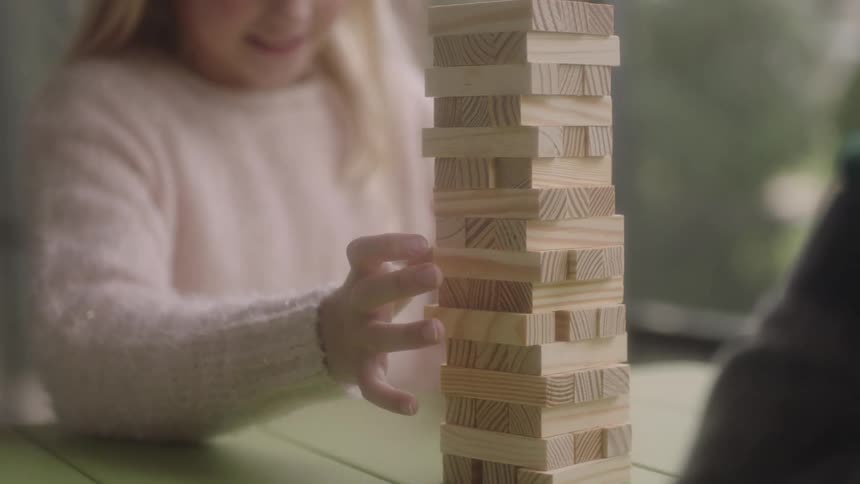 A young girl and other person play a game of jenga