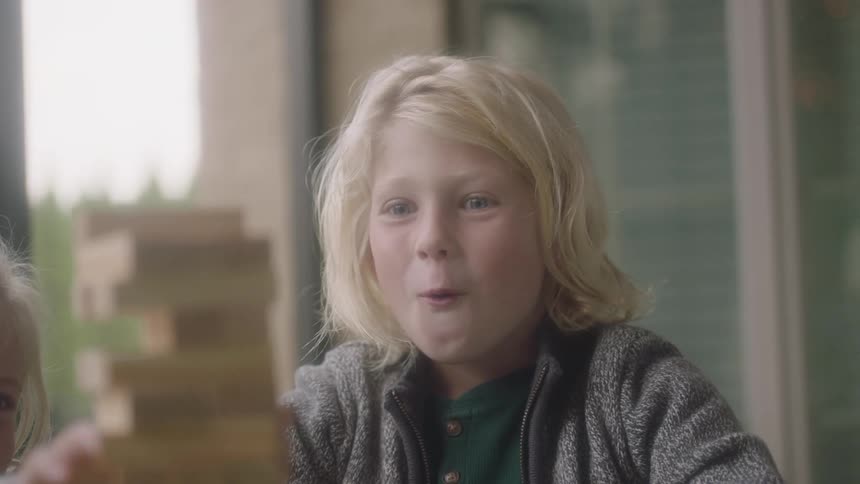 A boy plays a game with wooden pieces and is excited as he pulls a piece off the block