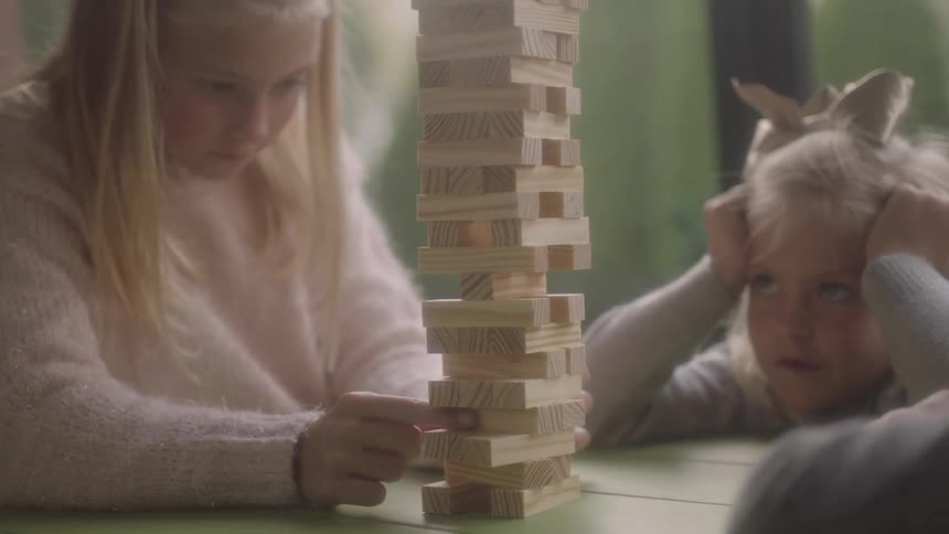 Children sit at a table and play a game with small wooden planks