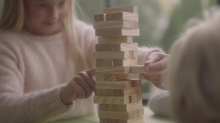 Girl plays wooden block game successfully removing piece from tower