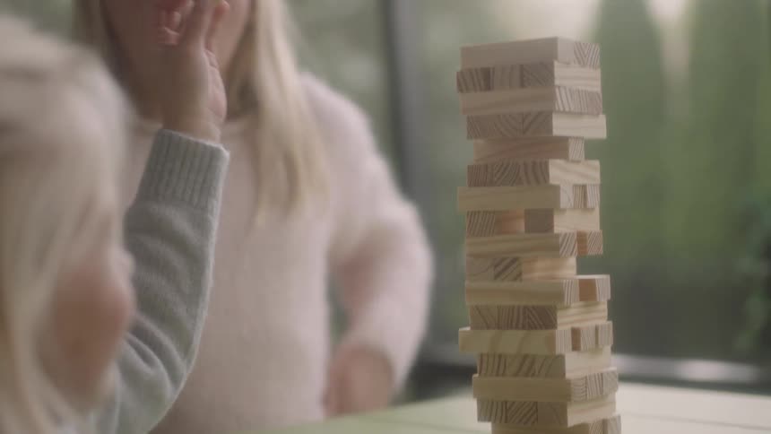 A young girl claps as her younger sister removes a wooden block from a stacking game
