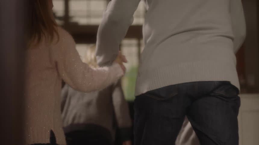 Daughters are greeting their dad at the door hugging and they hold hands and walk further into a room
