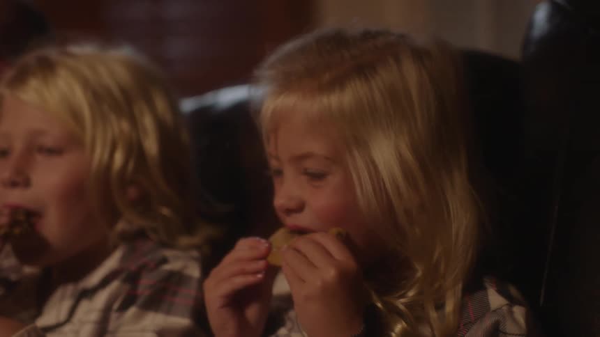 Children in a room sitting on a couch eating cookies