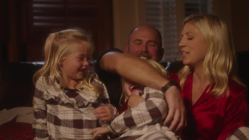 Two little girls laugh and sit on their mom and dads lap on a couch at home