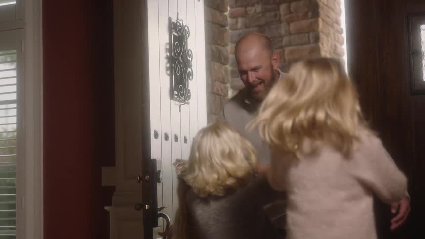 A man walks into the front door of his home greeted by his daughters running to him