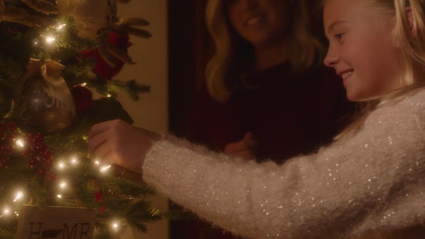 Mother and daughter decorate a christmas tree together at home