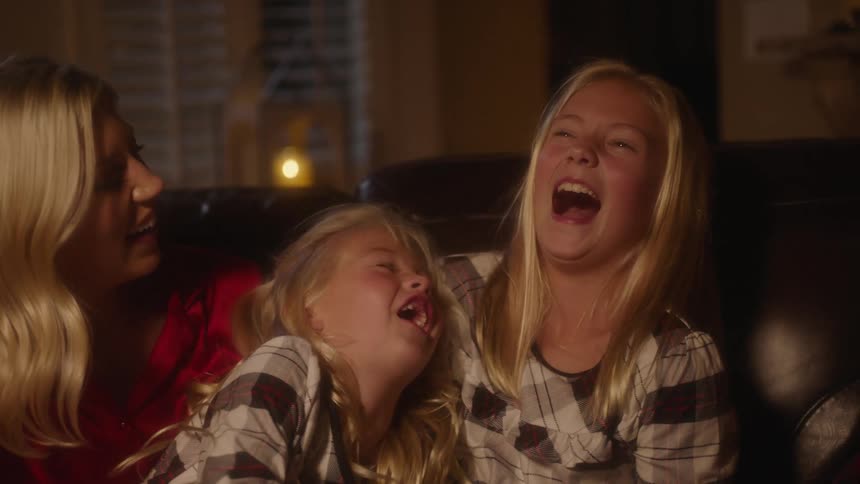 Two girls laughing when their mother tickles them on a couch in a dark living room