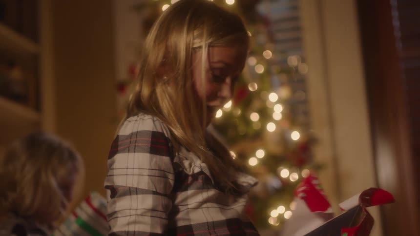 A blonde girl is unwrapping a gift and reveals a book as she smiles