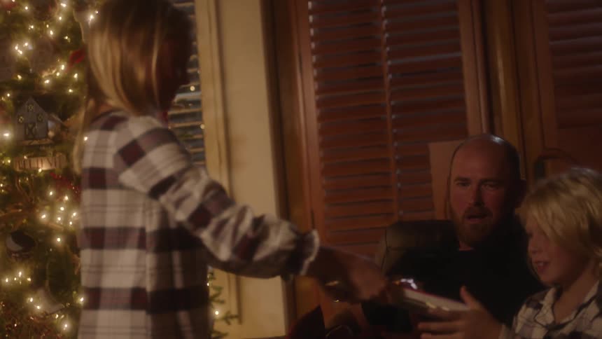Girl gives gift to sibling sitting on couch next to father