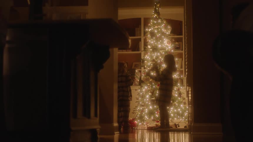 Three children pick up gifts under the christmas tree at night while in their pajamas