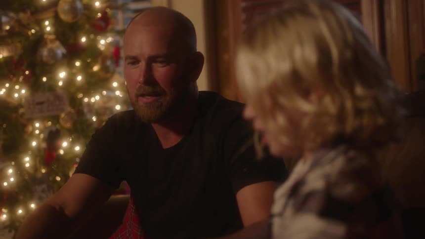 Man and child sit on a couch at night in front of a christmas tree