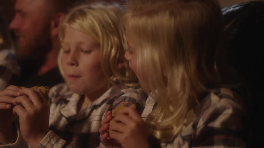 Two blonde siblings smle as they eat cookies while sitting next to their parents