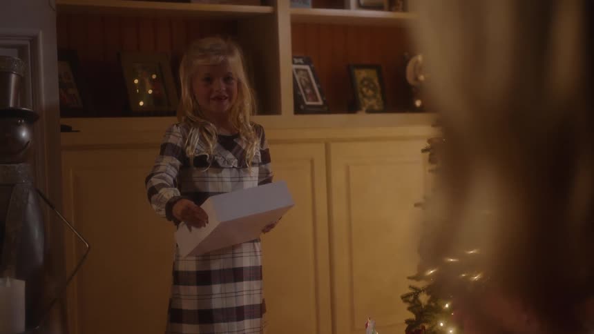Smiling child standing in a living room with a gift box in her hand