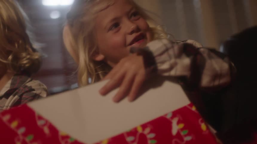 A young blonde girl smiles at her mother as she unwraps a present