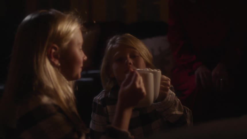Two blonde girls are sitting and clinking their white mugs inside at night