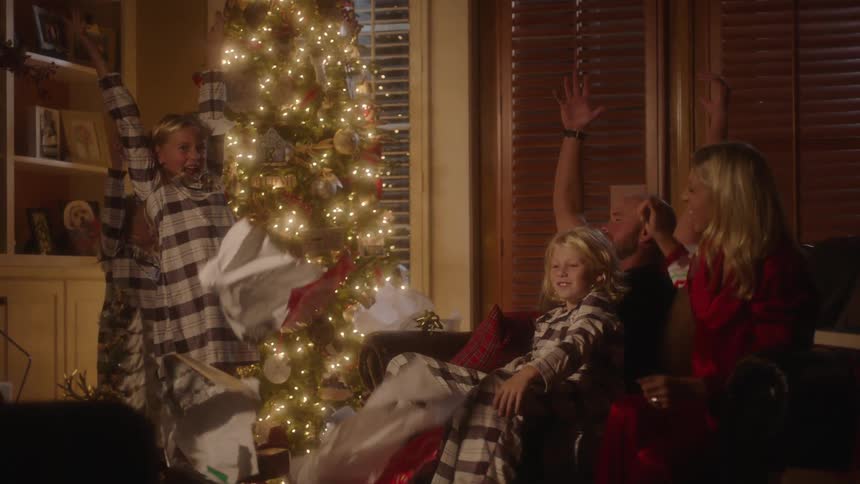 Family sitting in living room tossing gift wrapping paper up into the air sitting in front of a decorated christmas tree