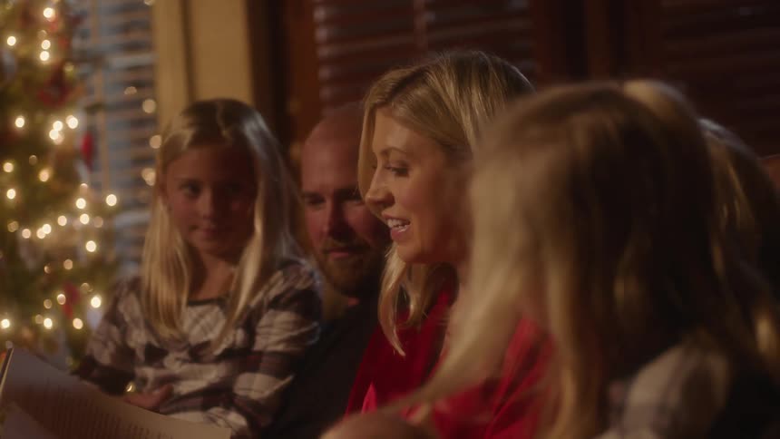 Family sitting on couch in living room listening to a mother read next to a christmas tree