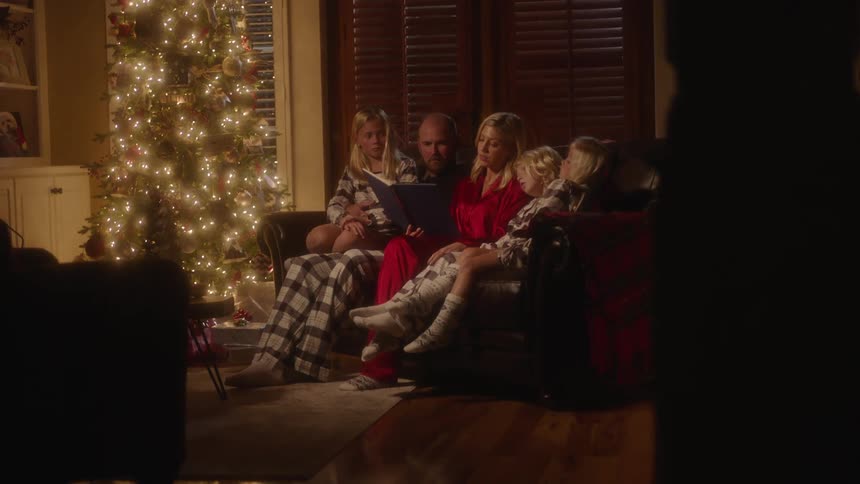 A family sitting in their living room listening to their mother read on the sofa