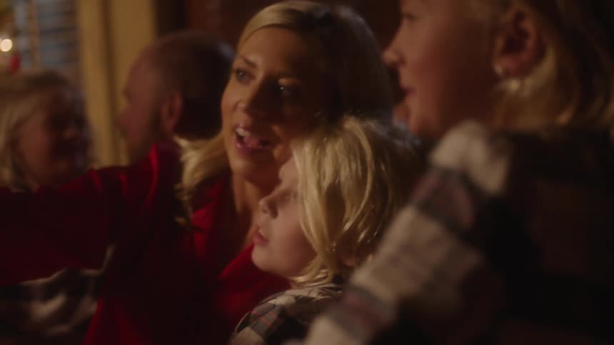 A family sits together on a couch talking and the mother looks at her cell phone