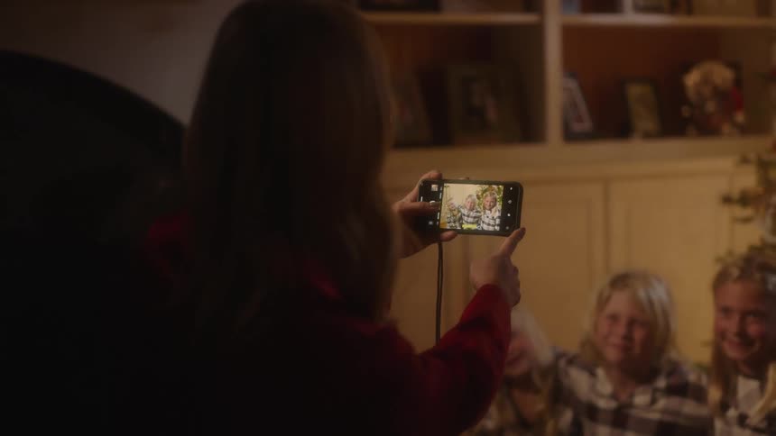Mother takes pictures of her daughters standing in front of the christmas tree with the smartphone in the living room at home