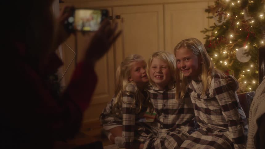 Person takes picture of siblings sitting in front of christmas tree